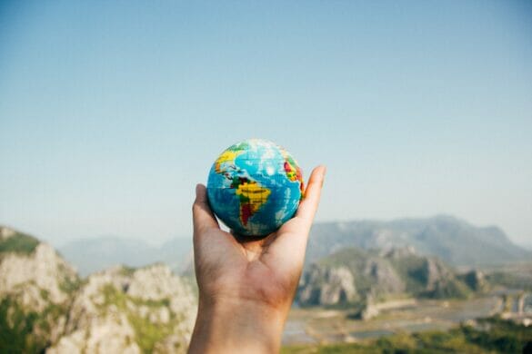 Hand holding up small earth with desert in the background