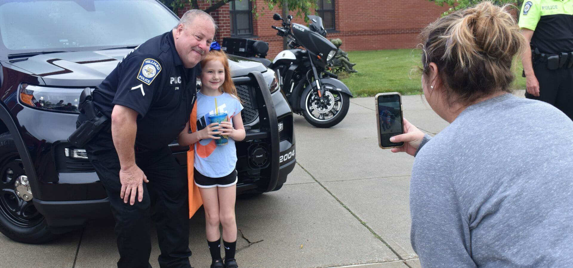 A girl posing in front of police cruiser with officer