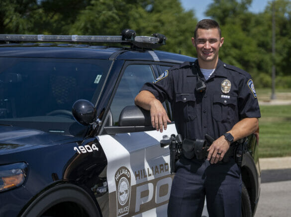A male officer standing in front of a police cruiser