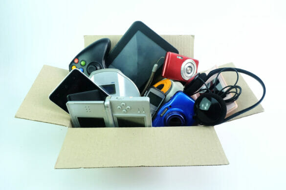 A box to be recycled, filled with various electronics, including handle held games, cameras, phones, and headphones.