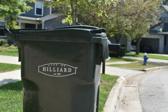 A close up shot of a black trashcan in front of houses