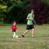 Man coaching little girl to kick soccer ball