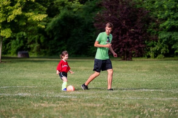 Man coaching little girl to kick soccer ball