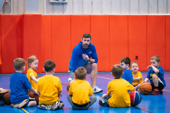 A coach talking to a group of young kids playing basketball
