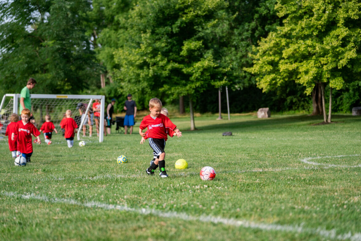 A little boy kicking a soccer ball while kids play soccer in the background