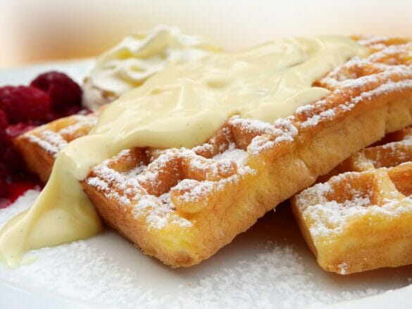 A closeup of waffles with cream, powder sugar, and fruit on them