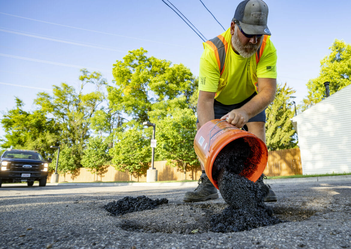 Public service worker pouring tar in a pot hole