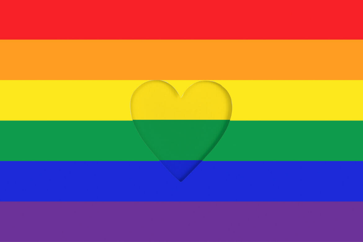 LGBTQ pride flag background. Rainbow Printed cardboard with die-cut heart shape. Top view