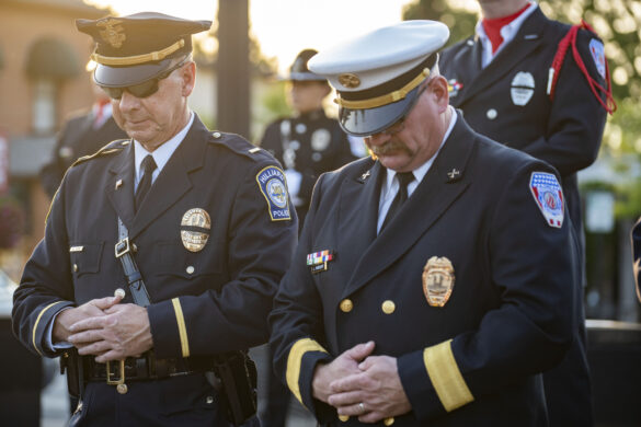 Police officer and firefighter in formal uniform bow their heads at First Responders Park.