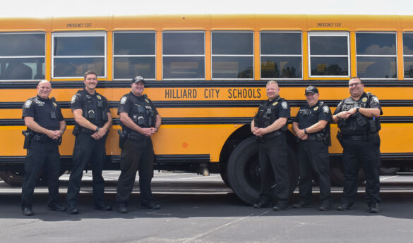 Team of six Hilliard school resource officers stand in front of a school bus