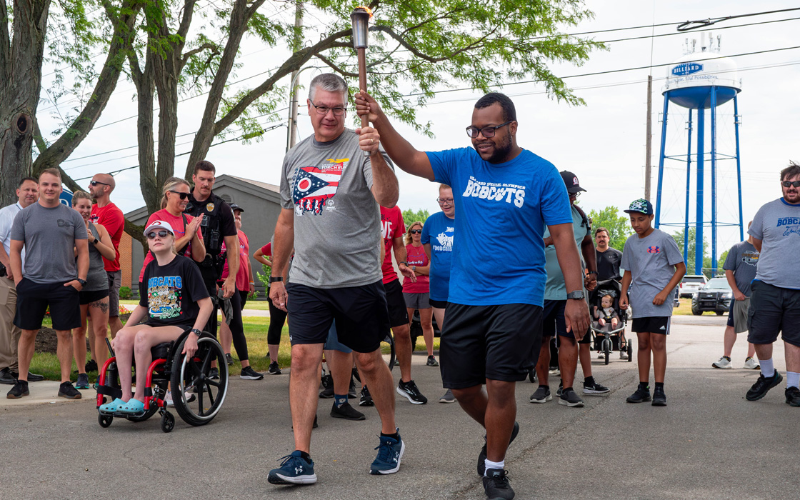 Photo of men and women running and walking while two people are carrying a torch