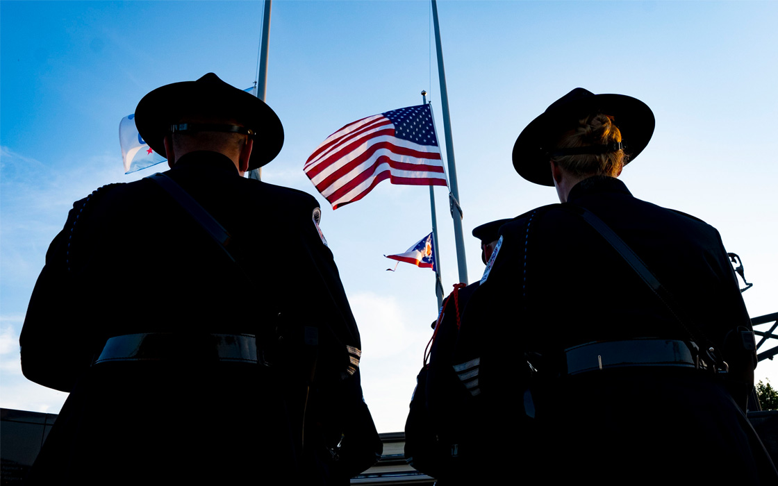 Silhouettes of police officers in front an American flag at half mass.