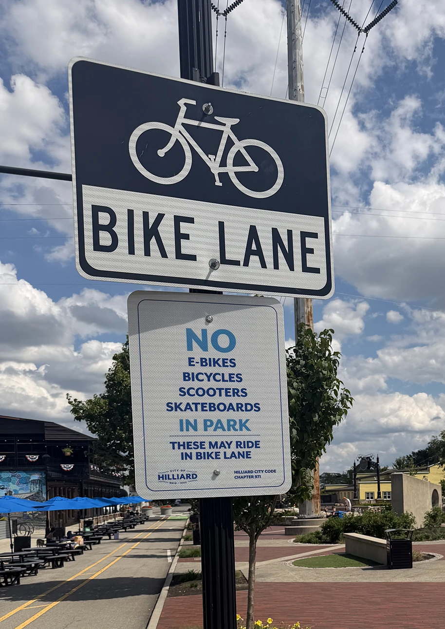 Two signs in Hilliard's Station Park announcing the bike lane and no E bikes, scooters, skateboards, and E Motos allowed in the parks