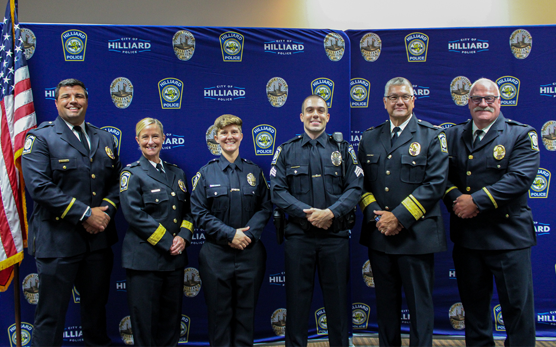 From left to right, Lt. Tyler Harris, Deputy Chief Kelly Weiner, Ofc. Kayla Martin, Sgt. Matt Hayes, Chief Michael Woods, and Lt. Doug Lightfoot pose for a photo in front of a backdrop with the City of Hilliard and Hilliard Division of Police logos.